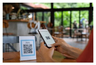 יד סורקת מדבקת QR על מעמד קטן ליד השולחן